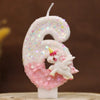 Vela blanca con forma de seis decorada con purpurina rosa y una pequeña figura de unicornio blanco.