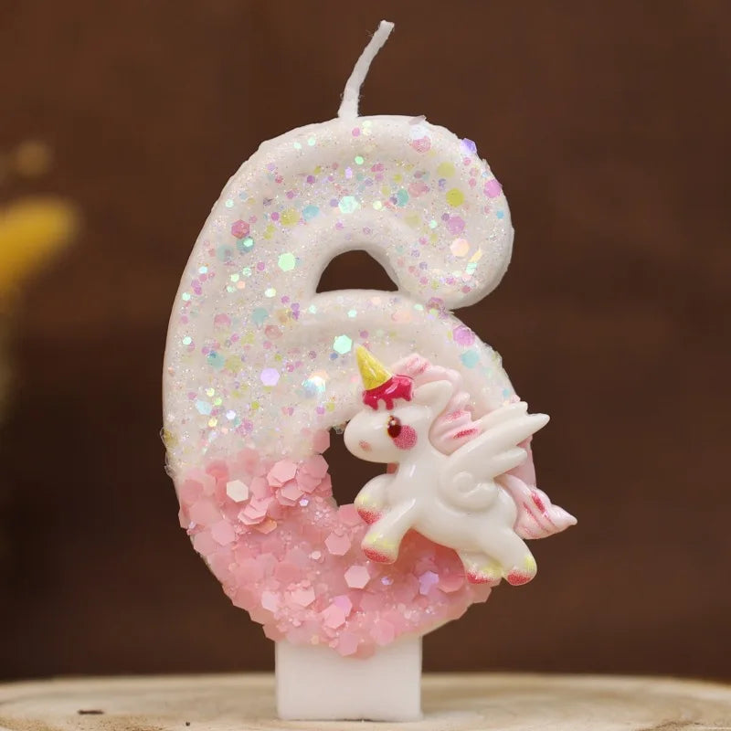 Vela blanca con forma de seis decorada con purpurina rosa y una pequeña figura de unicornio blanco.