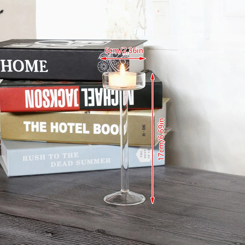 Elegant tall glass candle holder with a lit candle placed in front of a stack of books.