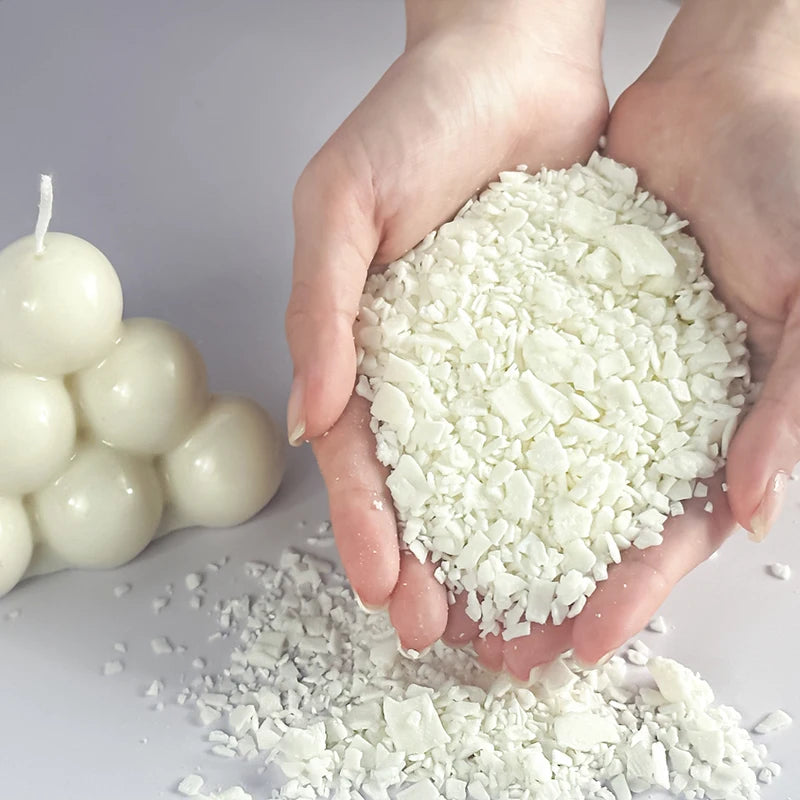 Hände halten einen Haufen weißer Sojawachsflocken neben einer Kerze.