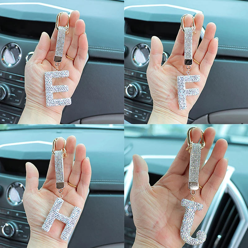 A set of crystal letter keychain charms spelling E, F, and H held in a person's hand.