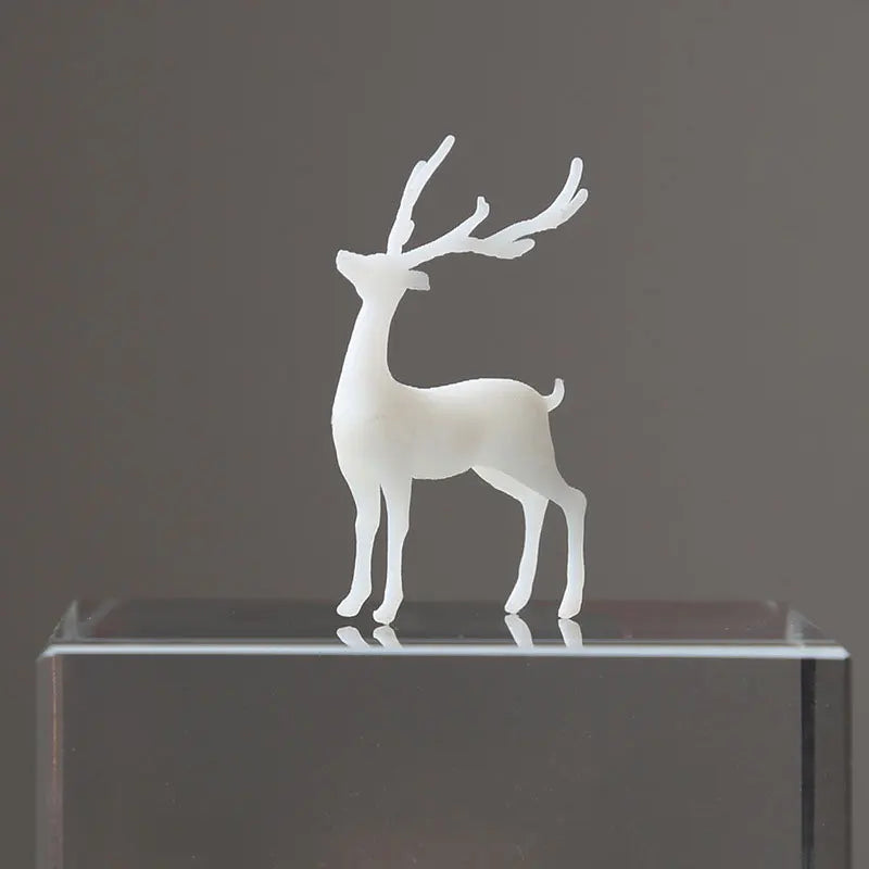 A white resin ornament of an elk deer with antlers standing on a clear glass base.