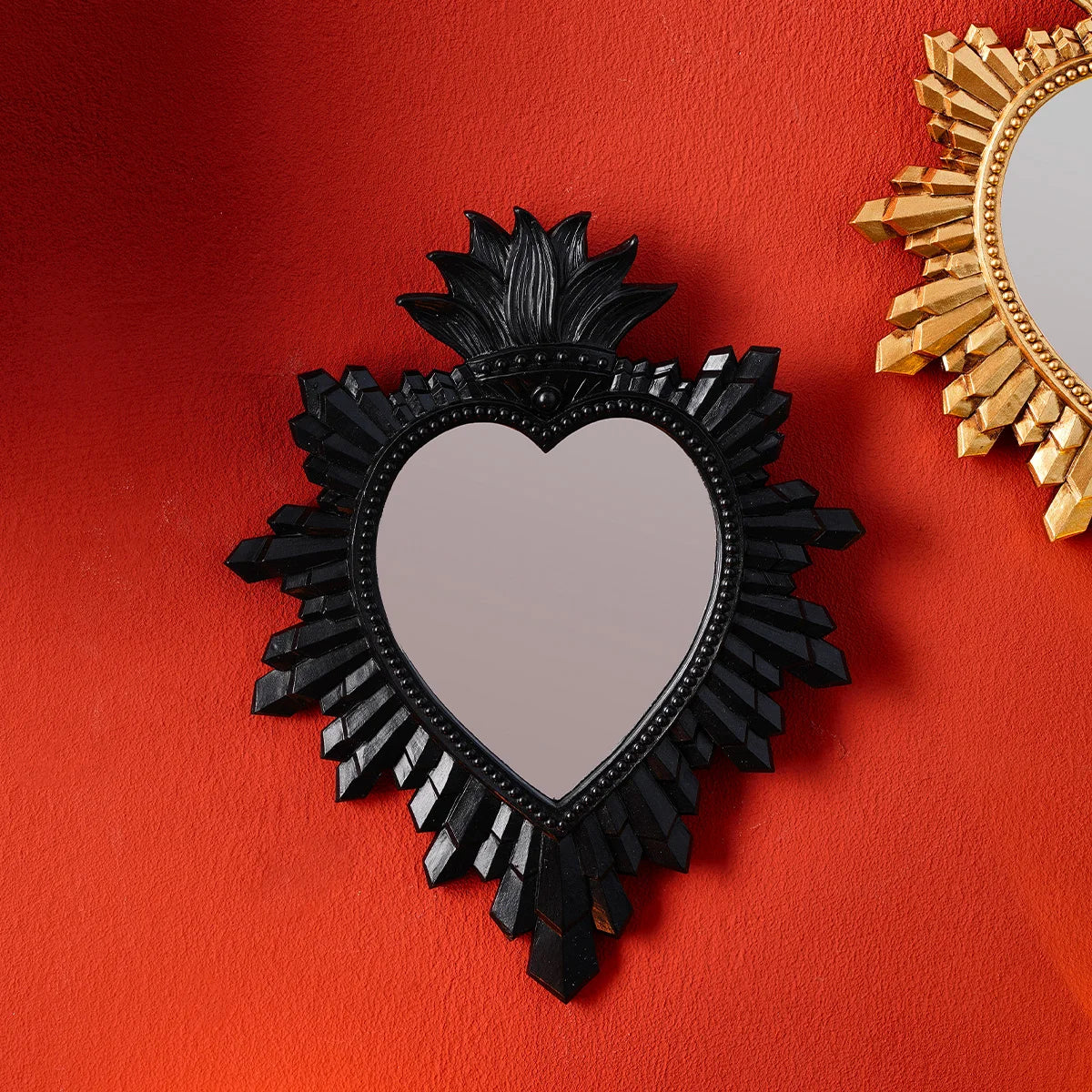 A black heart-shaped mirror pendant with a resin finish is displayed against an orange background next to a golden flame mirr