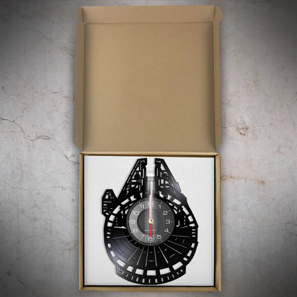 A vinyl record wall clock featuring a black face and a red and white second hand, displayed in its cardboard packaging.