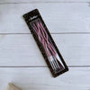 A package of long, thin pink spiral birthday candles is displayed on a white wooden surface.