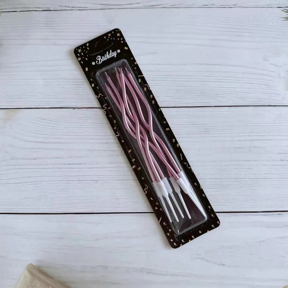 A package of long, thin pink spiral birthday candles is displayed on a white wooden surface.