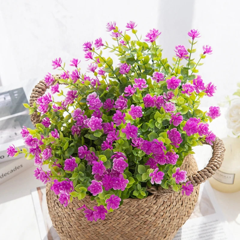 A vibrant faux plant featuring numerous purple flowers on green foliage, potted in a woven basket.