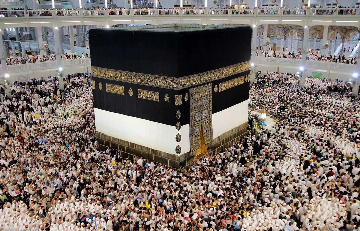 A large crowd of people surrounds a canvas wall art print depicting the Kaaba and Al Masjid An Nabawi.
