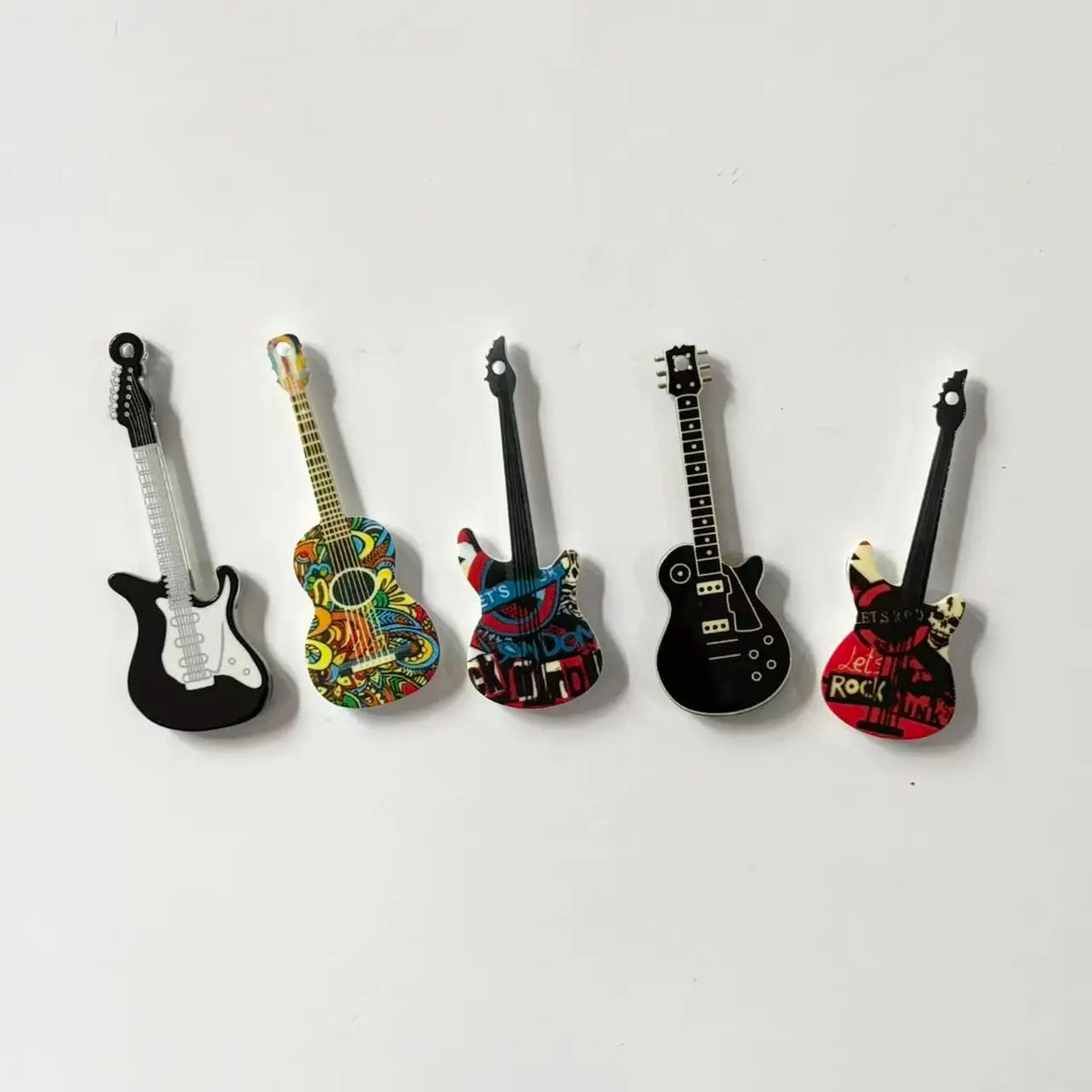 A set of five guitar-shaped fridge magnets in various colors and finishes.