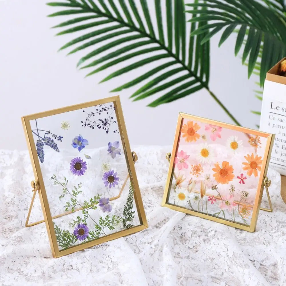 Two modern metal and acrylic photo frames with floral designs resting on a white lace fabric.