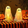 A set of glowing white ghost decorations displayed on a striped orange and black table with candy scattered around.