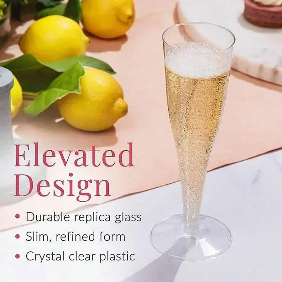 A tall, clear plastic replica champagne glass with a gold finish sits on a pink surface next to lemons.