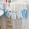 A decorative birthday garland spelling NEO made of white felt with blue ribbon accents
