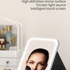 Miroir de maquillage pliable avec écran numérique montrant le visage d'une femme et un pinceau sur une surface blanche.