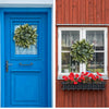 A bright blue door with a wreath of green eucalyptus and a red flower box on a wooden house.
