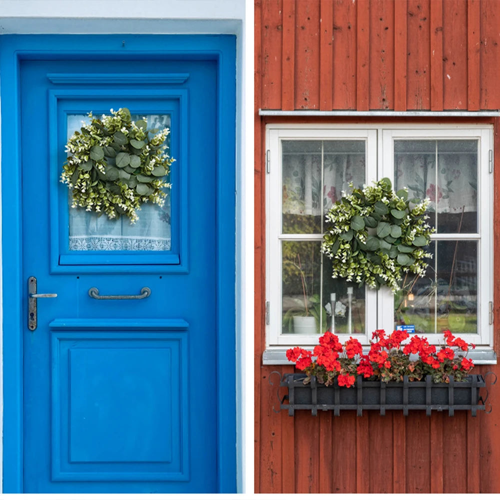 A bright blue door with a wreath of green eucalyptus and a red flower box on a wooden house.