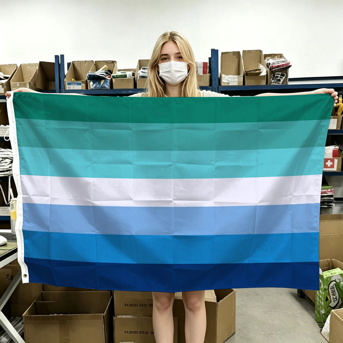 A blonde woman holds up a horizontal Pride flag banner with six horizontal stripes of teal, white, and blue.