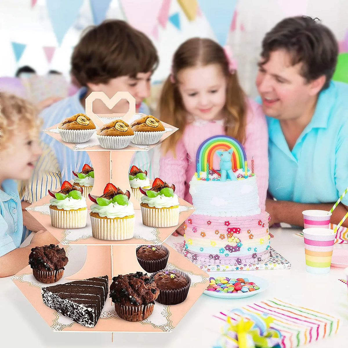 A 3-tier rainbow cupcake stand displaying various cupcakes and desserts for a party display.