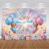 A pink and blue gender reveal backdrop featuring gold lettering, balloons, and floral accents against a soft sky background.