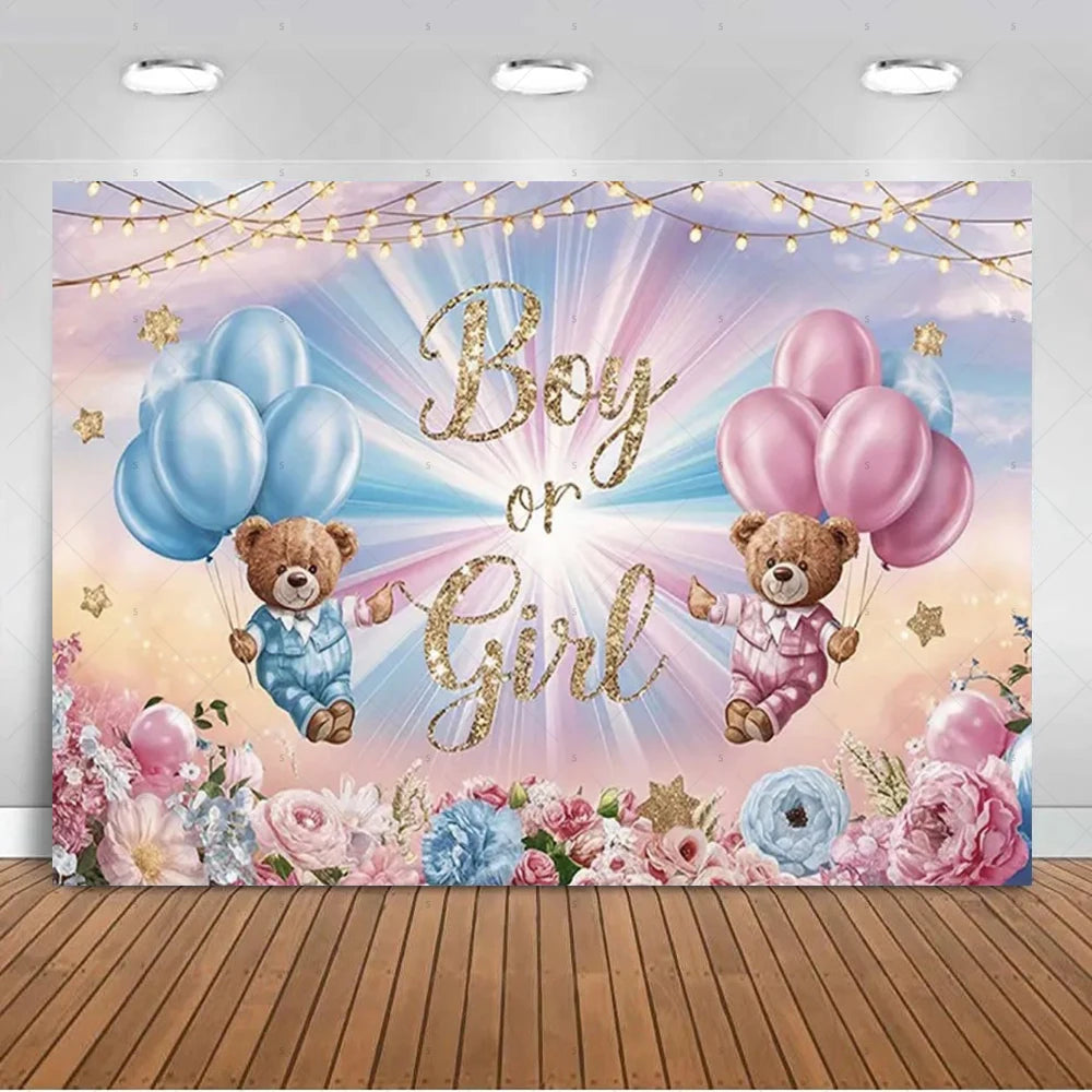 A pink and blue gender reveal backdrop featuring gold lettering, balloons, and floral accents against a soft sky background.