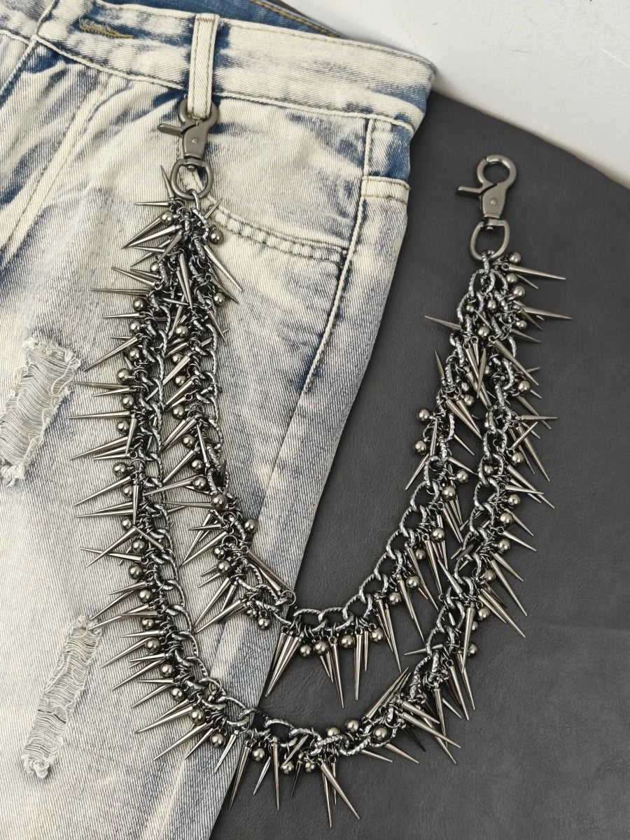 A silver and black spiked chain keychain is displayed against a background of light wash denim jeans.