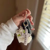 A hand holds a bohemian woven cross car keychain featuring a white fluffy animal charm.