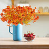 A vibrant orange artificial autumn bouquet in a blue mug sits on a wooden table.