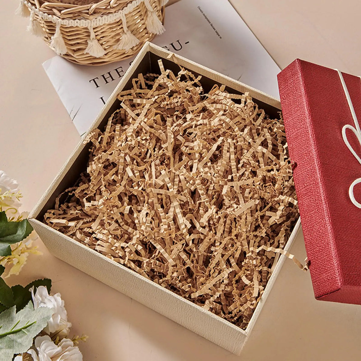 A wooden box filled with crinkle cut paper shred filler next to a red gift box.