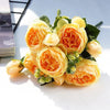 A bouquet of orange and cream silk rose and peony artificial flowers with green leaves.