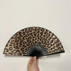 A black and brown leopard print folding hand fan is shown open against a white background.