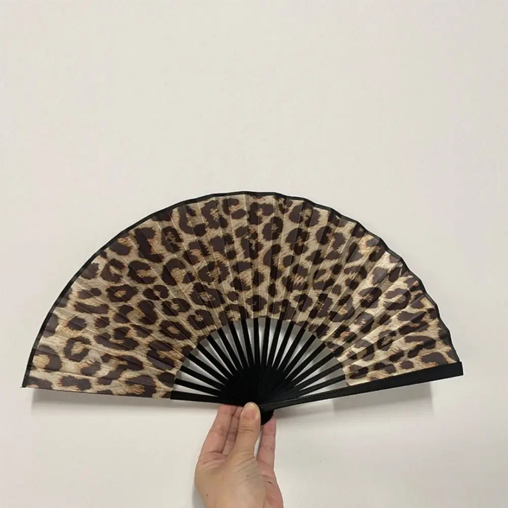 A black and brown leopard print folding hand fan is shown open against a white background.