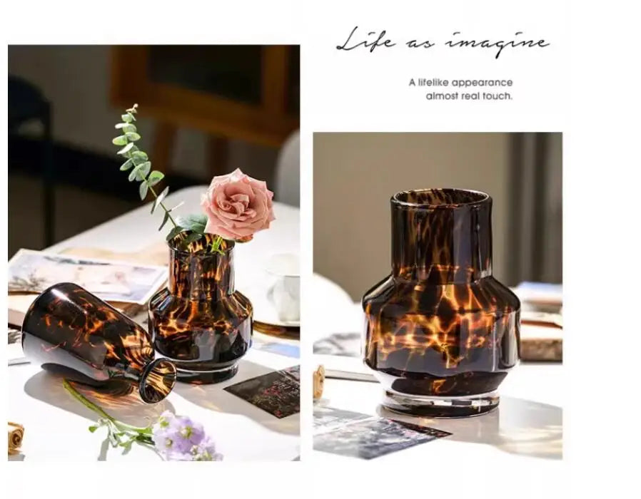 A dark amber leopard print glass vase with a pink rose and greenery on a white table.