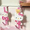 A pink and white cartoon cat hook with a yellow cat charm hanging on a white cabinet door.