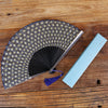 A titanium alloy folding hand fan with a patterned silk cover and a light blue fabric insert resting on a wooden surface.