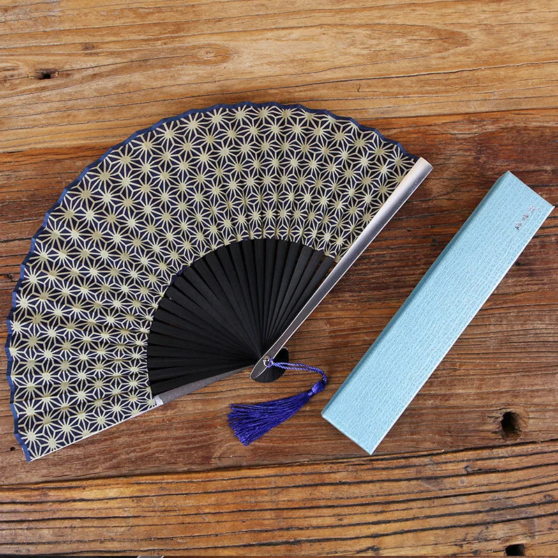A titanium alloy folding hand fan with a patterned silk cover and a light blue fabric insert resting on a wooden surface.