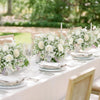 A close-up of a white floral centerpiece arrangement featuring roses and baby's breath on a white table setting.