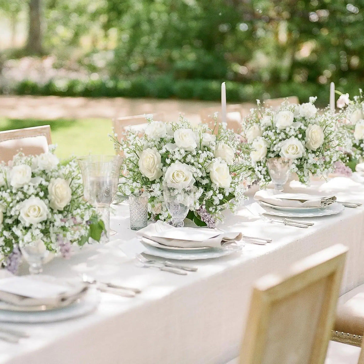 A close-up of a white floral centerpiece arrangement featuring roses and baby's breath on a white table setting.