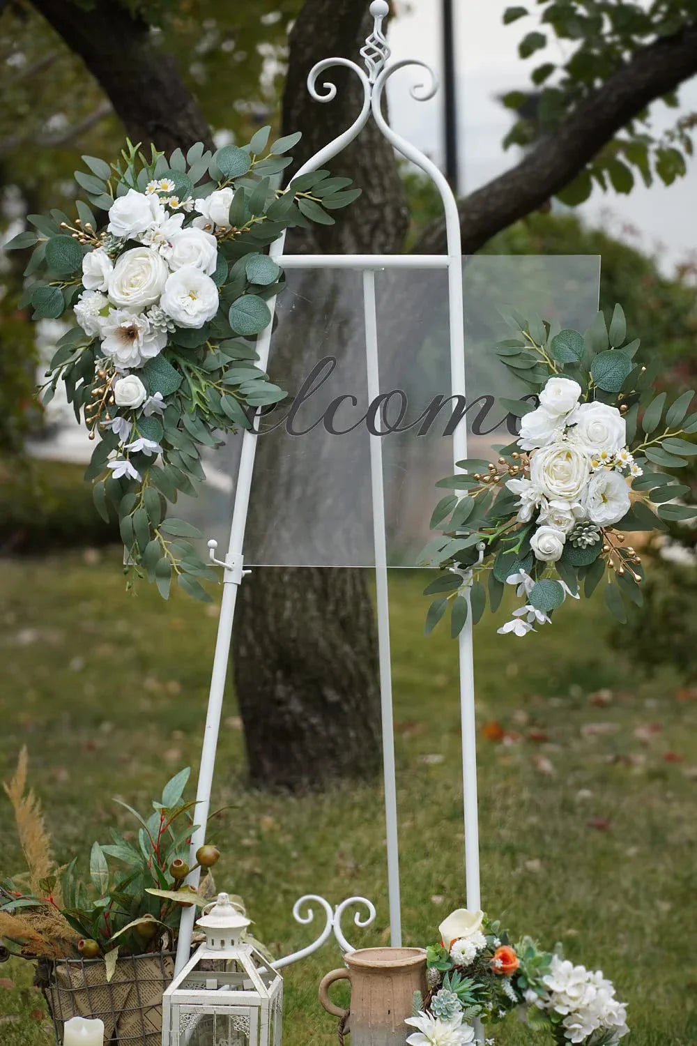 A white metal wedding arch decorated with white roses and green eucalyptus foliage in an outdoor setting.