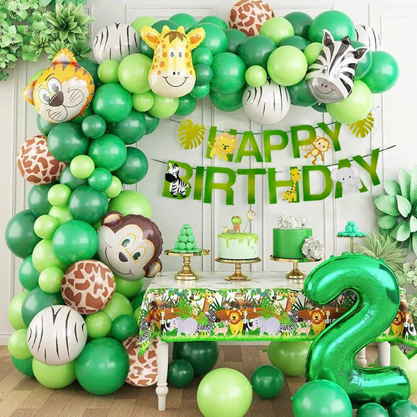 A green and white balloon garland arch decorated with safari animals and palm leaves for a birthday party.