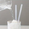 Clear disposable drinking straws are being poured into a glass container.