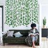 A green artificial ivy vine garland covers a white wall behind a dark green sofa and wooden floor.
