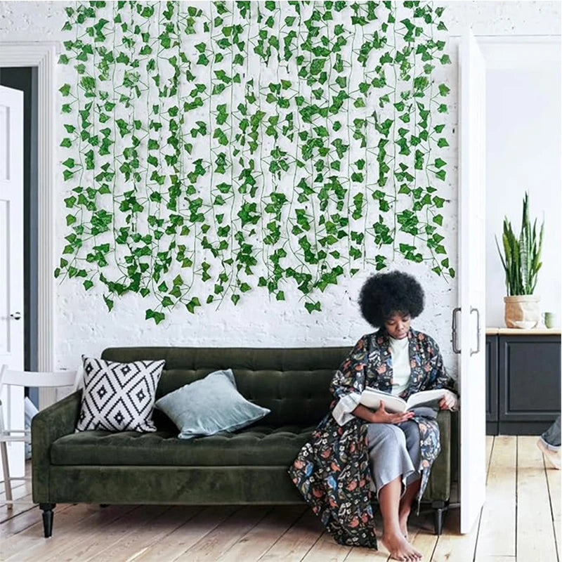 A green artificial ivy vine garland covers a white wall behind a dark green sofa and wooden floor.