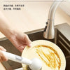 A hand is using an adjustable long-handled liquid washing brush to clean a plate in a kitchen sink.