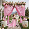Pink fabric backdrop curtains framing a couple at an outdoor event with floral arrangements and greenery