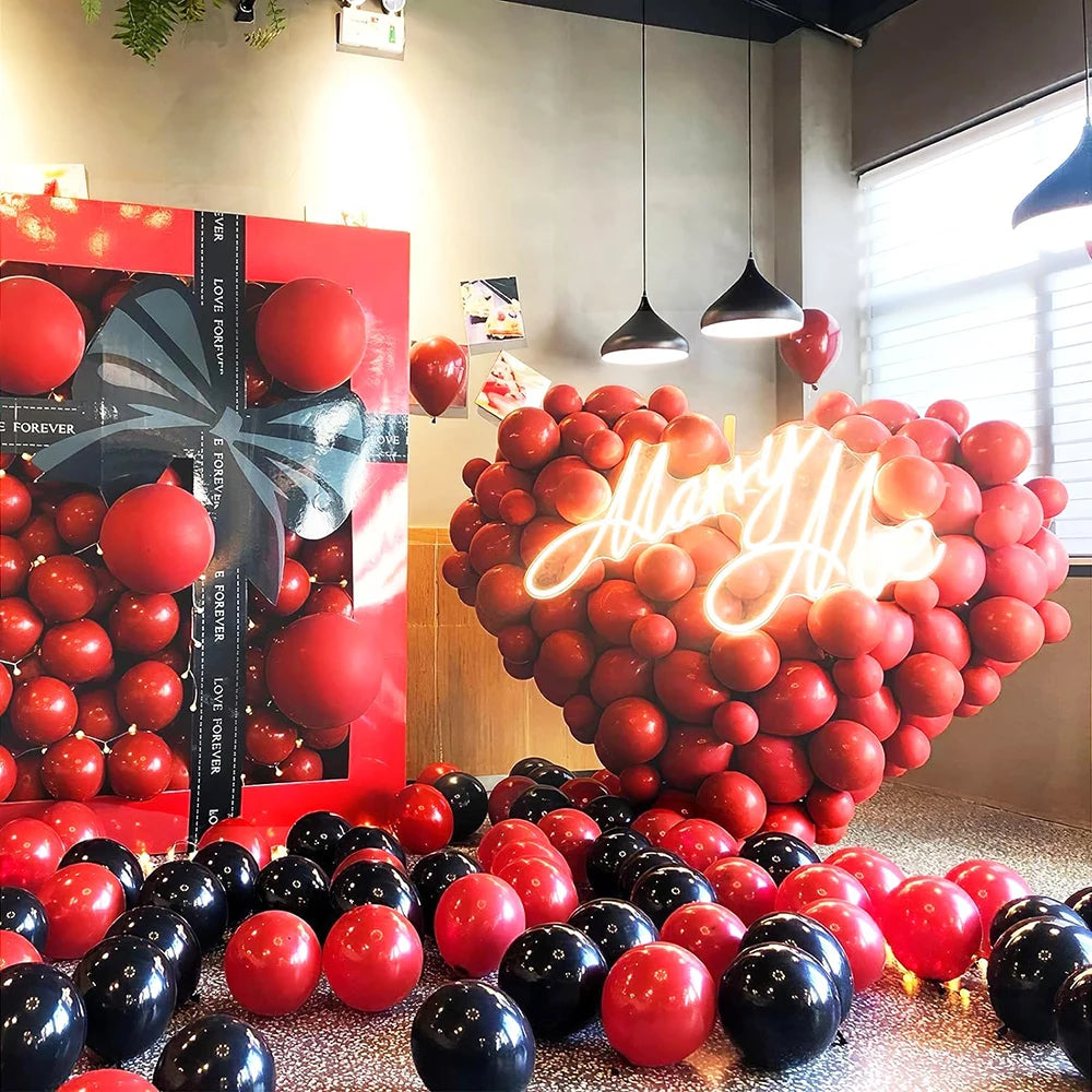 A large arrangement of round latex balloons in red and black colors is displayed indoors.