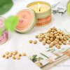 A natural soy wax travel candle in a gold tin with a lit wick and grapefruit scent surrounded by loose wax pellets.