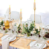 A set of three gold metal taper candle holders with white candles displayed on a wooden table setting.