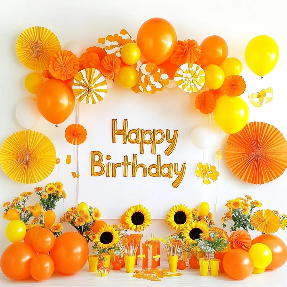 A colorful arrangement of orange and yellow latex balloons and flowers celebrating a happy birthday.