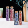 Five glass bottles filled with various colored crystals including purple, pink, blue, and amber stones