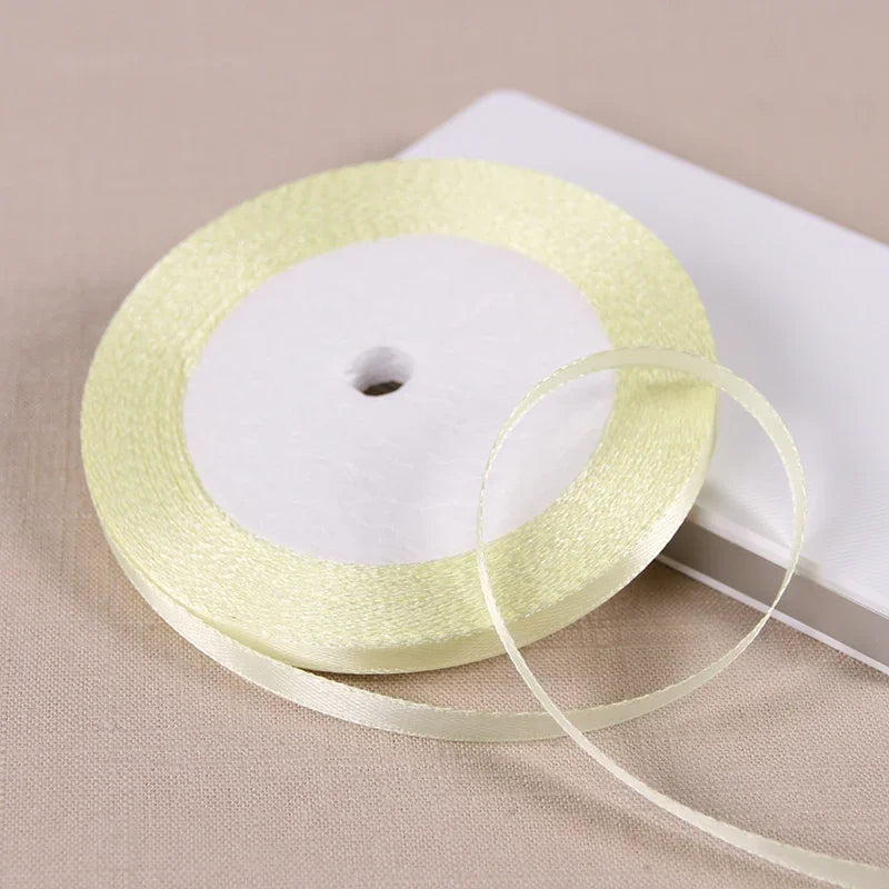 A roll of pale yellow satin ribbon is shown on a white box, ready for gift wrapping or crafts.